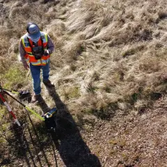 Geodeta w kamizelce odblaskowej z aparaturą GPS przy płocie.