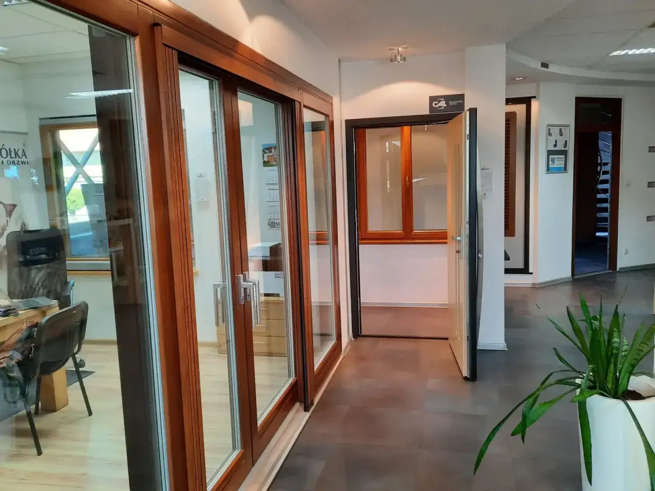 Salon z oknami i drzwiami drewnianymi, z otwartymi drzwiami i rośliną w doniczce.
