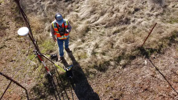 Geodeta w kamizelce odblaskowej z aparaturą GPS przy płocie.